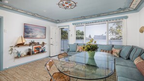 Un salón con una mesa de centro de vidrio, sofá azul y un cuadro en la pared.