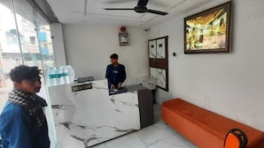 A reception area with a marble counter, a red bench, and a framed picture on the wall. - Hotel Shree Kedar Palace (Ujjain)