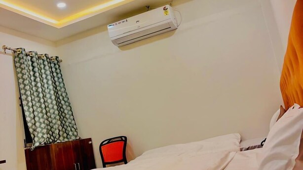 A hotel room with a bed, a ceiling fan, an air conditioning unit, a desk with a chair, and a curtain. - Hotel Shree Kedar Palace (Ujjain)