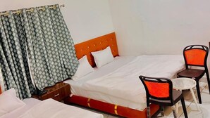 A hotel room with two beds, a ceiling fan, an air conditioner, and a small table with chairs. - Hotel Shree Kedar Palace (Ujjain)