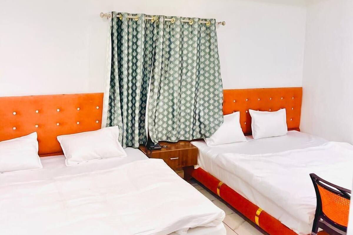A hotel room with two beds, a ceiling fan, and a window with patterned curtains.