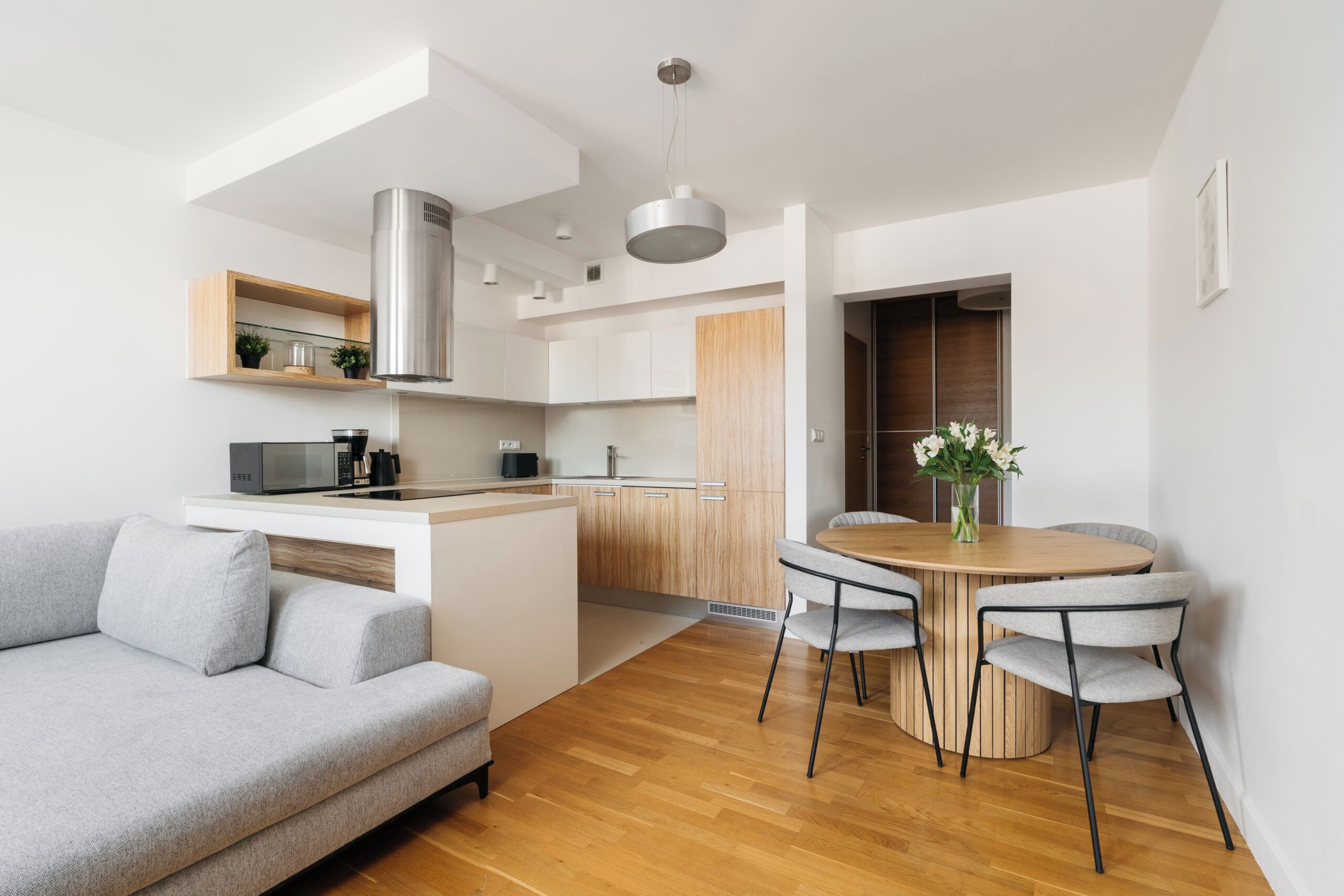 Una cocina moderna con estufa integrada, microondas y cafetera. Hay una zona de comedor con una mesa redonda y cuatro sillas.