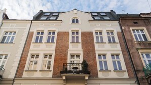 Ein mehrstöckiges Gebäude mit einer symmetrischen Fassade, das einen zentralen Balkon mit Tisch und Stühlen sowie eine Reihe von Fenstern in jeder Etage zeigt.