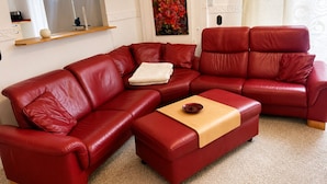 A red leather sectional sofa with a wooden coffee table, a painting on the wall, and a window with curtains.