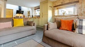 Un salon chaleureux avec deux canapés, une cuisine à l’arrière-plan et un mur en pierre.