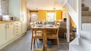 Un coin repas avec une table et des chaises en bois, une cuisine équipée d’un four à micro-ondes et un escalier menant à un autre niveau.