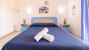 Een netjes opgemaakt bed met een blauw hoofdbord, twee nachtkastjes met decoratieve objecten, en een aan de muur hangend schilderij.