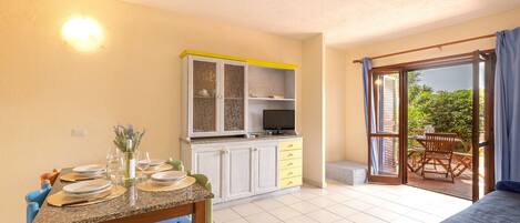 Een compacte kamer met een eethoek, een kitchenette en een glazen schuifdeur naar een terras.