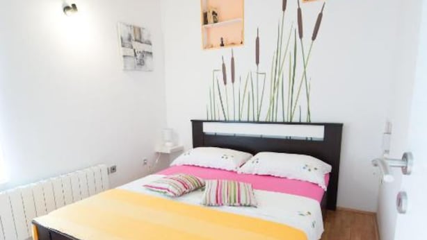Une chambre à coucher comprenant un lit, des tables de chevet, un radiateur et une étagère murale agrémentée d’objets décoratifs.