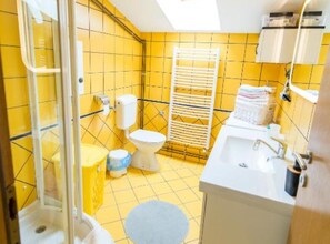 A bathroom with yellow tiled walls, a white toilet, a sink, and a shower area. - Apartments Galić (Ploce)