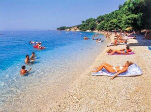 A pebbled beach with clear blue water, people swimming and sunbathing. - Apartments Galić (Ploce)
