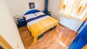 Une chambre à coucher avec un lit, une table de chevet, une lampe, un radiateur et une fenêtre avec des rideaux.