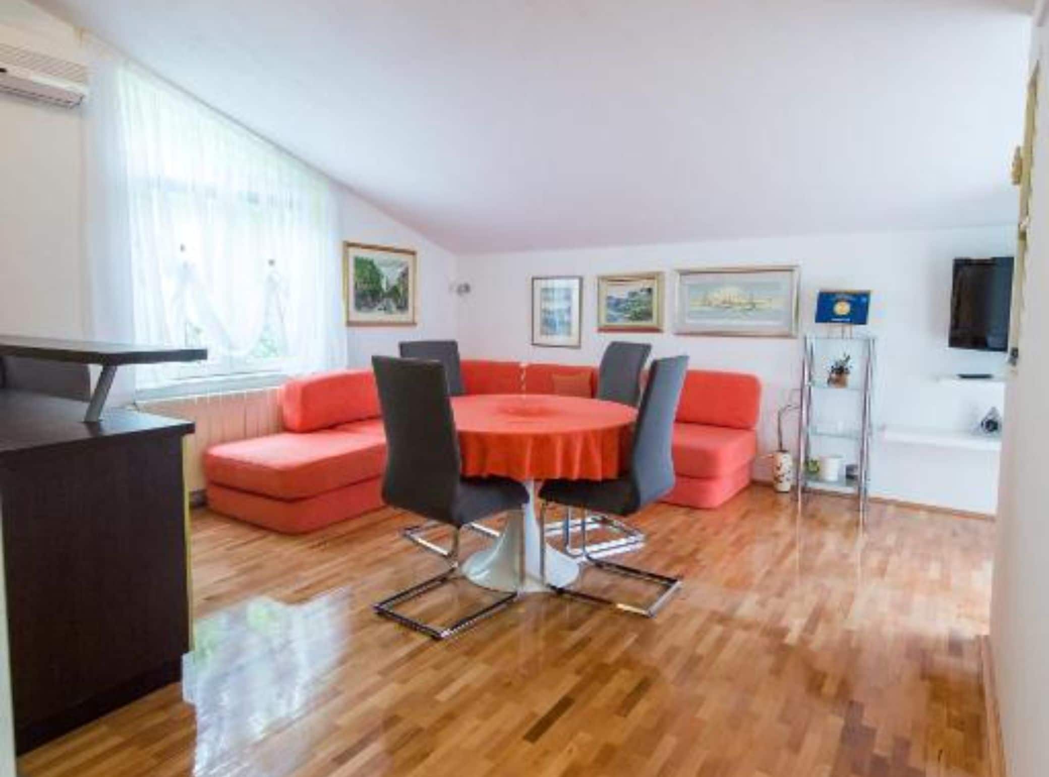 Een moderne woonkamer met een ronde tafel, rode banken en een televisie aan de muur.