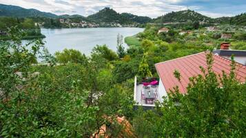 A view of a lake with a red-roofed building in the foreground, surrounded by greenery and hills in the background.