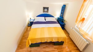 Une petite chambre à coucher, bien éclairée, avec un lit, des tables de chevet, un miroir et un radiateur.