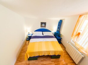 A small, brightly lit bedroom with a bed, bedside tables, a mirror, and a radiator. - Apartments Galić (Ploce)