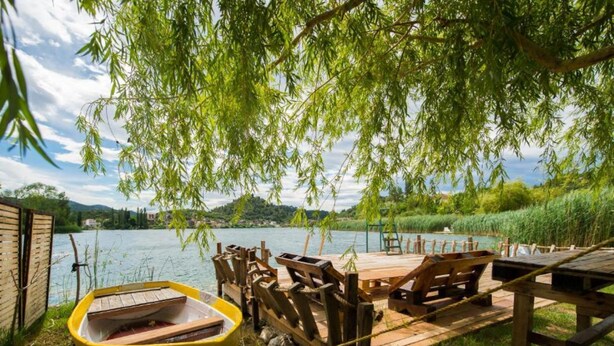 A wooden dock with a yellow boat, wooden benches, and a table under a willow tree by a lake. - Apartments Galić (Ploce)