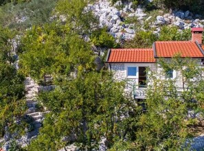A stone house with a red-tiled roof surrounded by greenery and rocks. - Apartments Galić (Ploce)