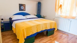 Une chambre à coucher comprenant un lit, une table de chevet, une commode, une fenêtre avec des rideaux et un radiateur.