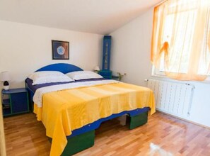 A bedroom with a bed, a nightstand, a dresser, a window with curtains, and a radiator. - Apartments Galić (Ploce)