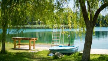 A wooden bench and a small boat with a ladder by a calm lake, surrounded by trees.