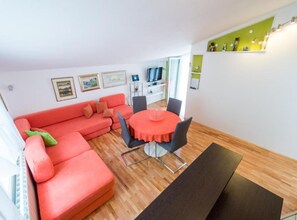 A modern living room with a red sofa, a round table, and a TV in the background. - Apartments Galić (Ploce)