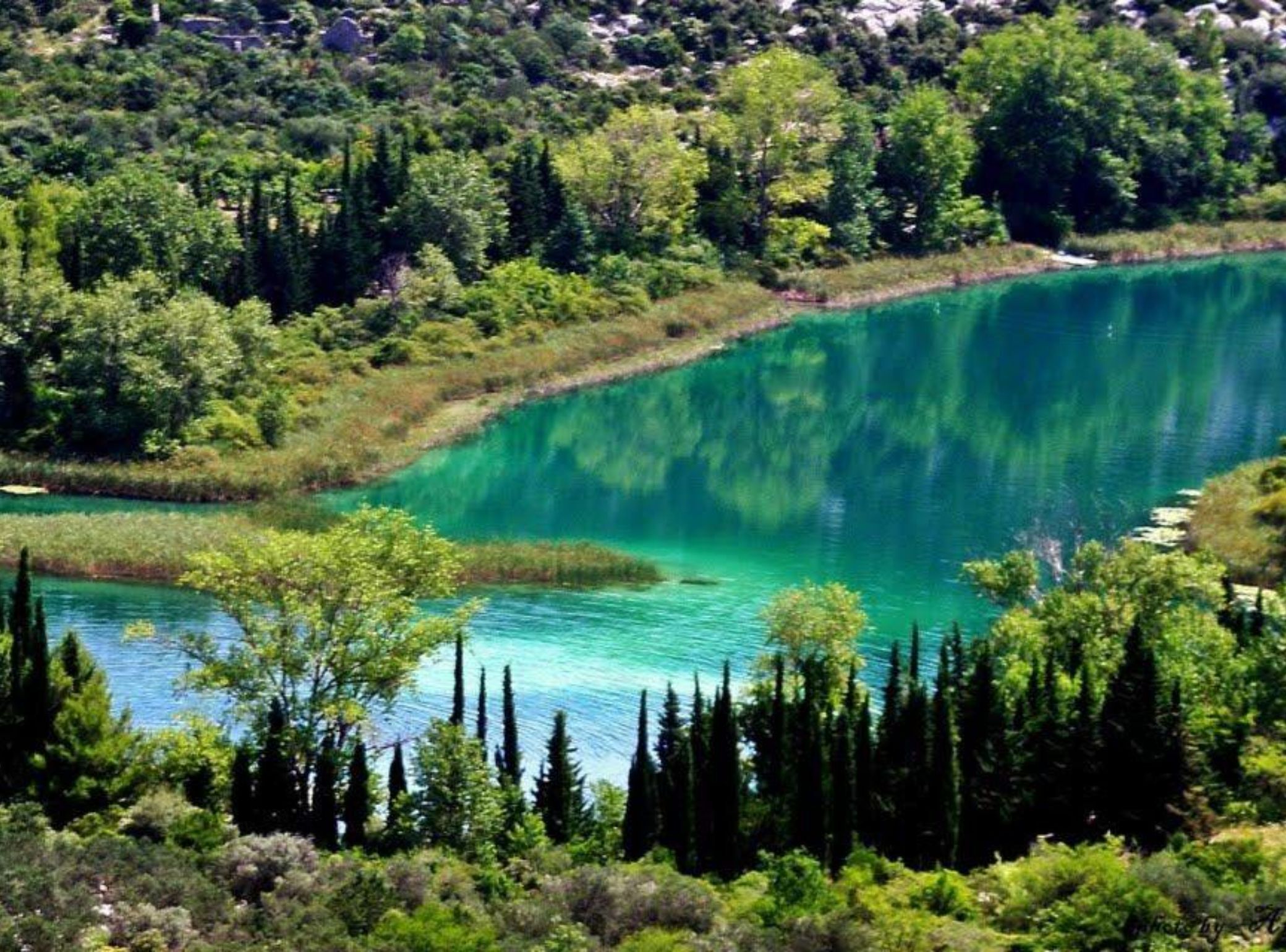 A natural landscape with a clear turquoise lake surrounded by dense greenery and trees.