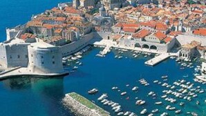 An aerial view of a historic coastal town with a fortified castle, narrow streets, and a marina filled with boats. - Apartments Galić (Ploce)