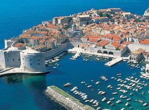 An aerial view of a historic coastal town with a fortified castle, narrow streets, and a marina filled with boats. - Apartments Galić (Ploce)