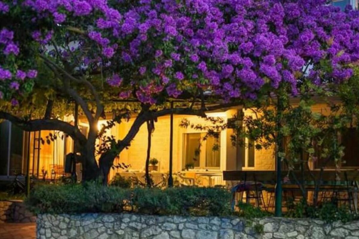 A building with a stone wall and a tree with purple flowers.