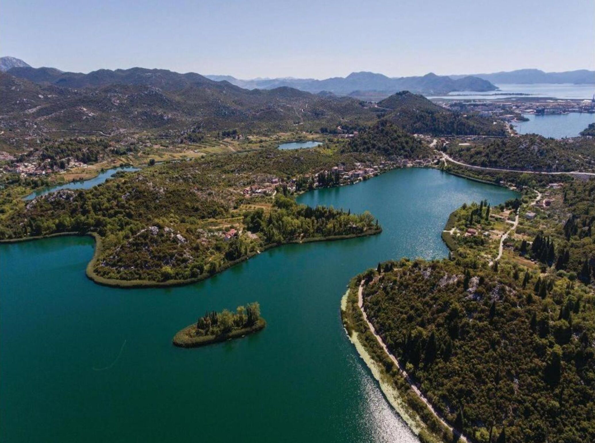 An aerial view of a coastal area with a large body of water, surrounded by hills and a small island.