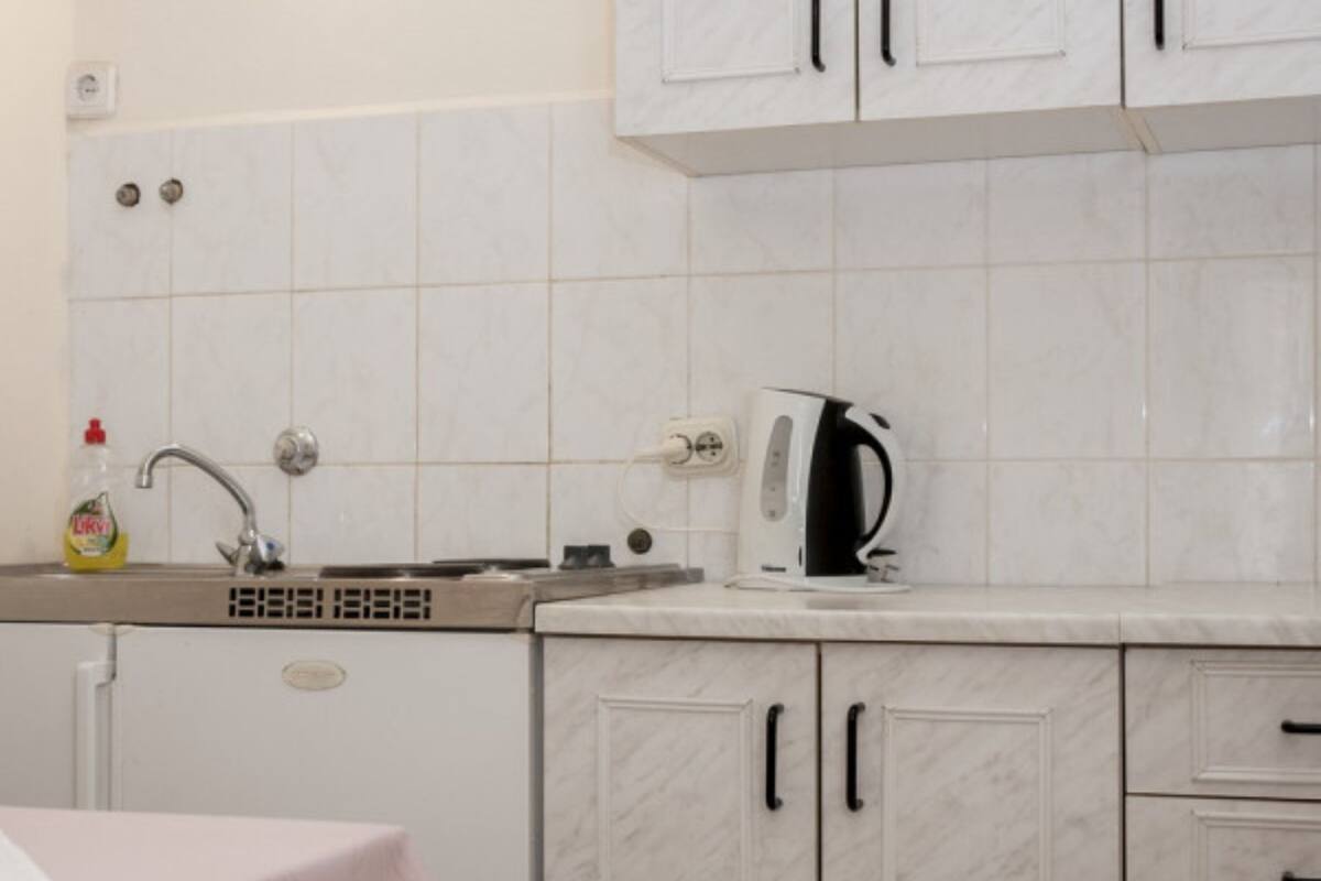 Una cucina con mobili bianchi, un lavello con rubinetto, un bollitore e un tavolo con tovaglia rosa.