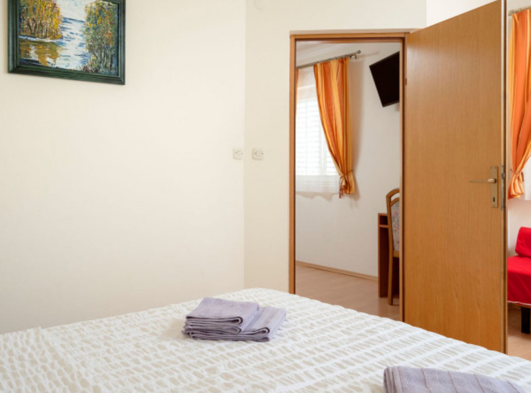 Una habitación de hotel con una cama, un cuadro en la pared y una puerta que da a otra estancia.