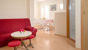 Ein Wohnzimmer mit einem roten Sofa, einem runden Tisch mit einer Vase und einem Essbereich mit Tisch und Stühlen.