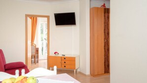 Ein Zimmer mit einem Bett, einem an der Wand montierten Fernseher, einem Holzschrank und einem Fenster mit Vorhängen.