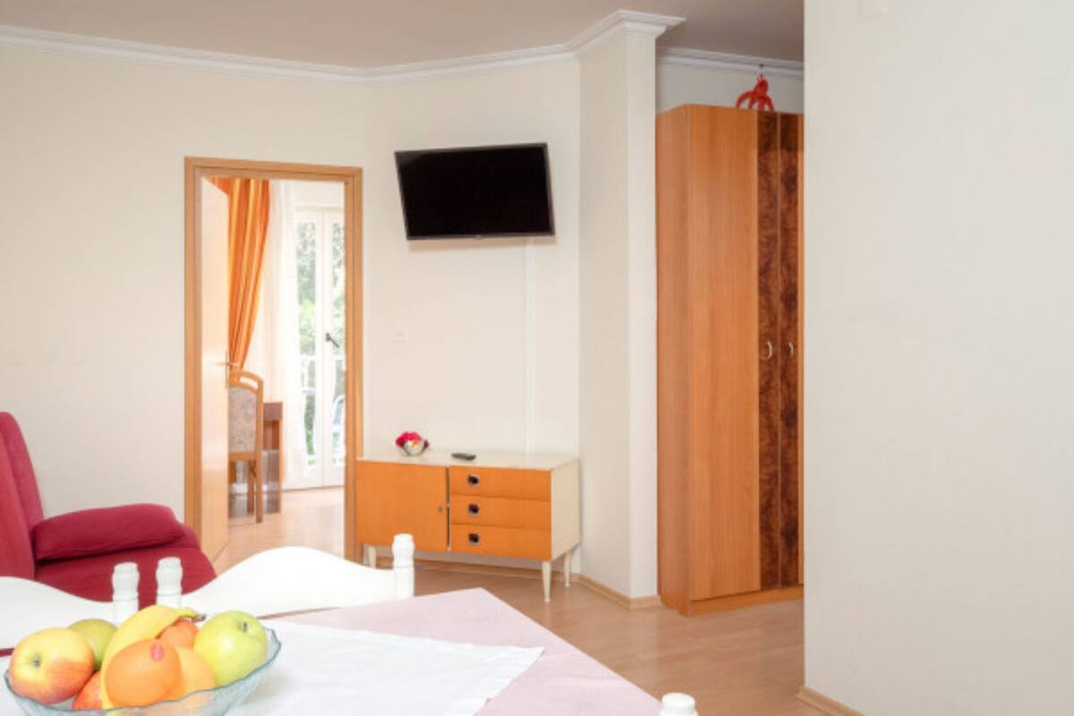 Una stanza con un letto, una TV a parete, un armadio in legno e una finestra con tende.