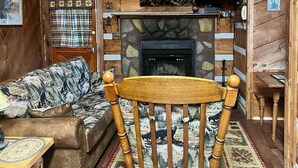 Un salon chaleureux avec une cheminée en pierre, des rideaux à carreaux et un téléviseur fixé au-dessus.