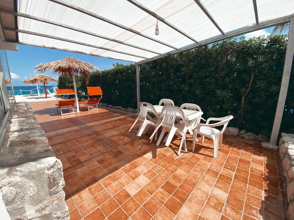 An outdoor patio with a tiled floor, white plastic chairs, and a table.