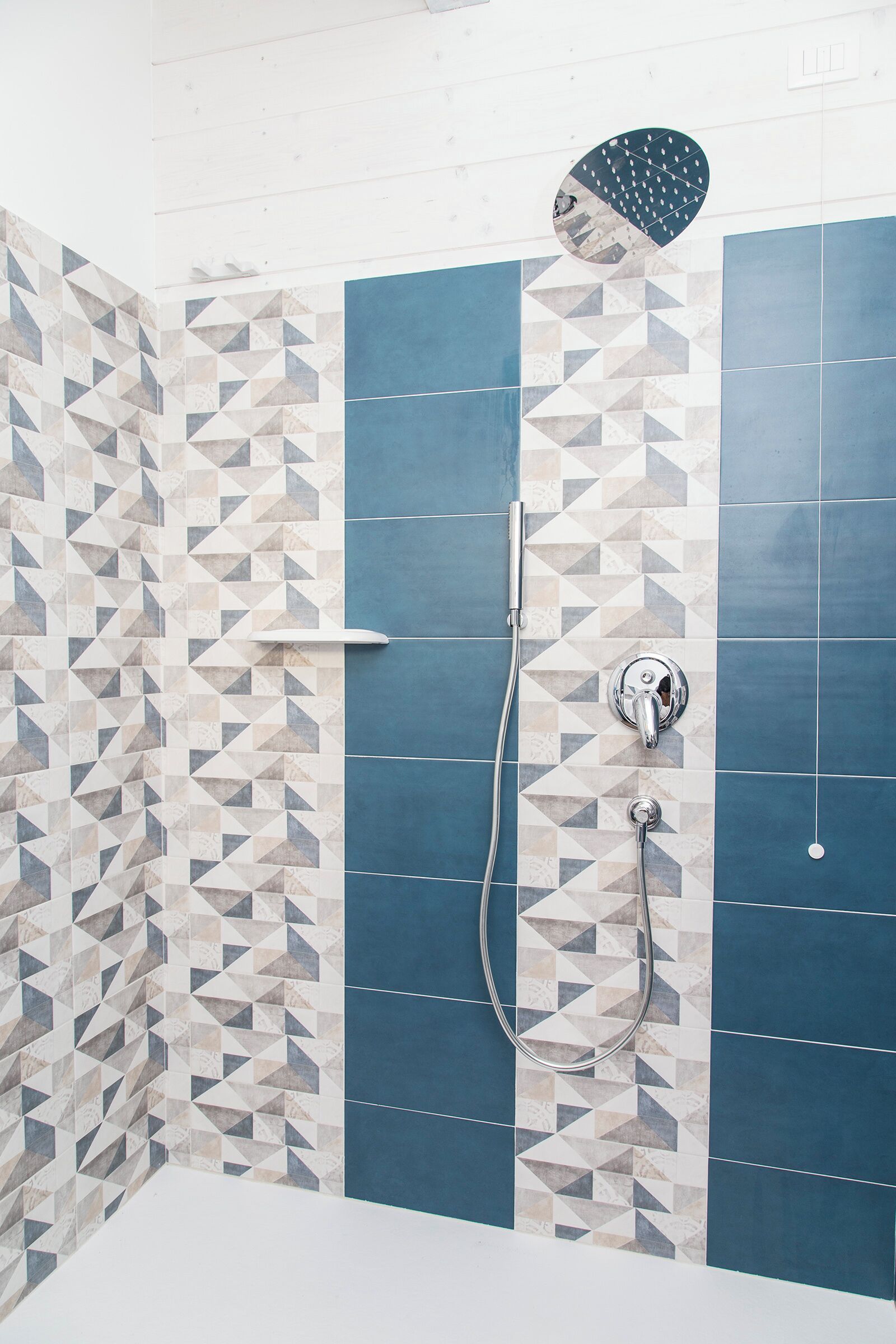 A shower area with blue and beige patterned tiles, a handheld showerhead, and a wall-mounted faucet.