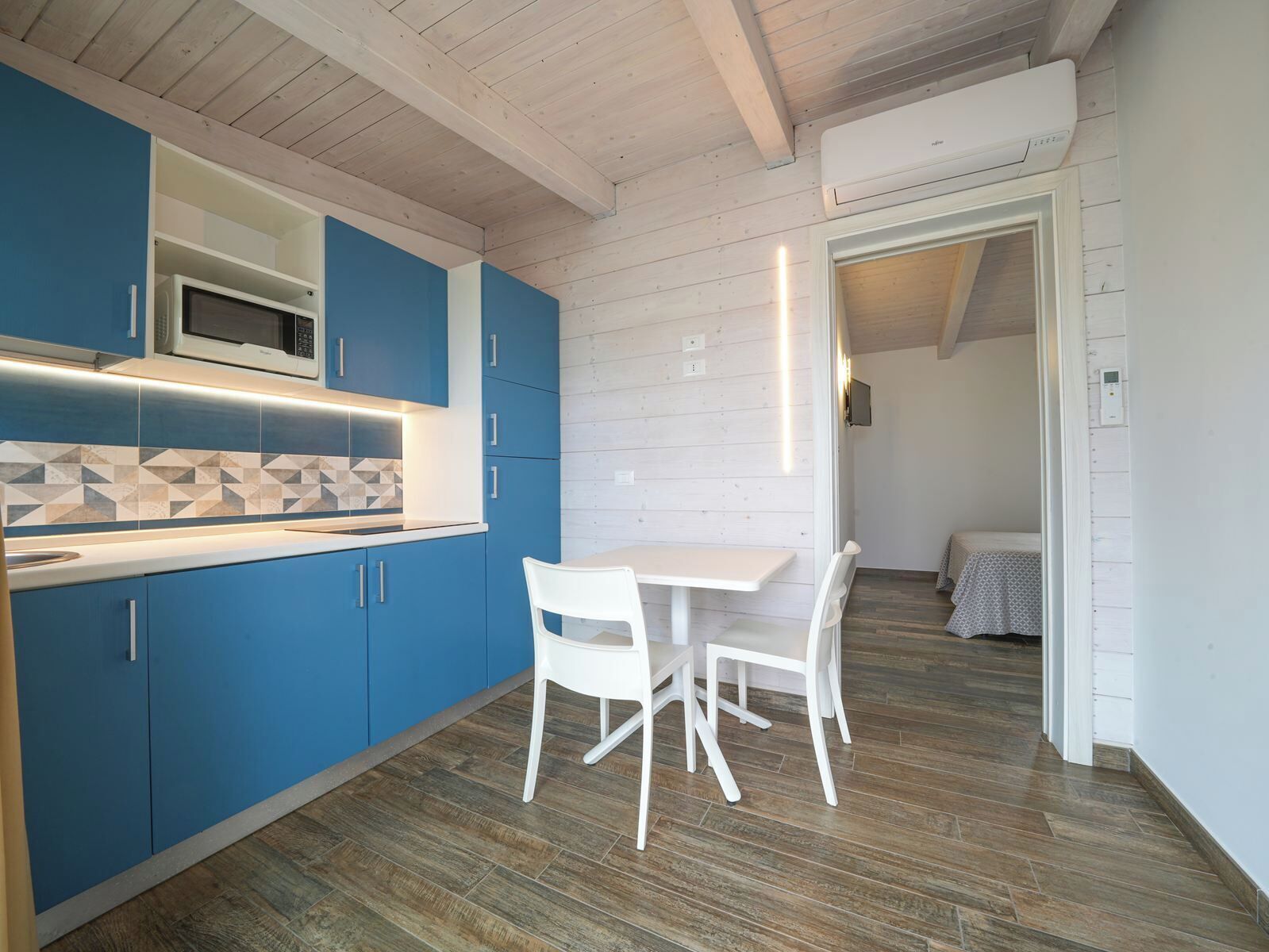 A modern kitchen with blue cabinets, a white dining table, and a microwave.