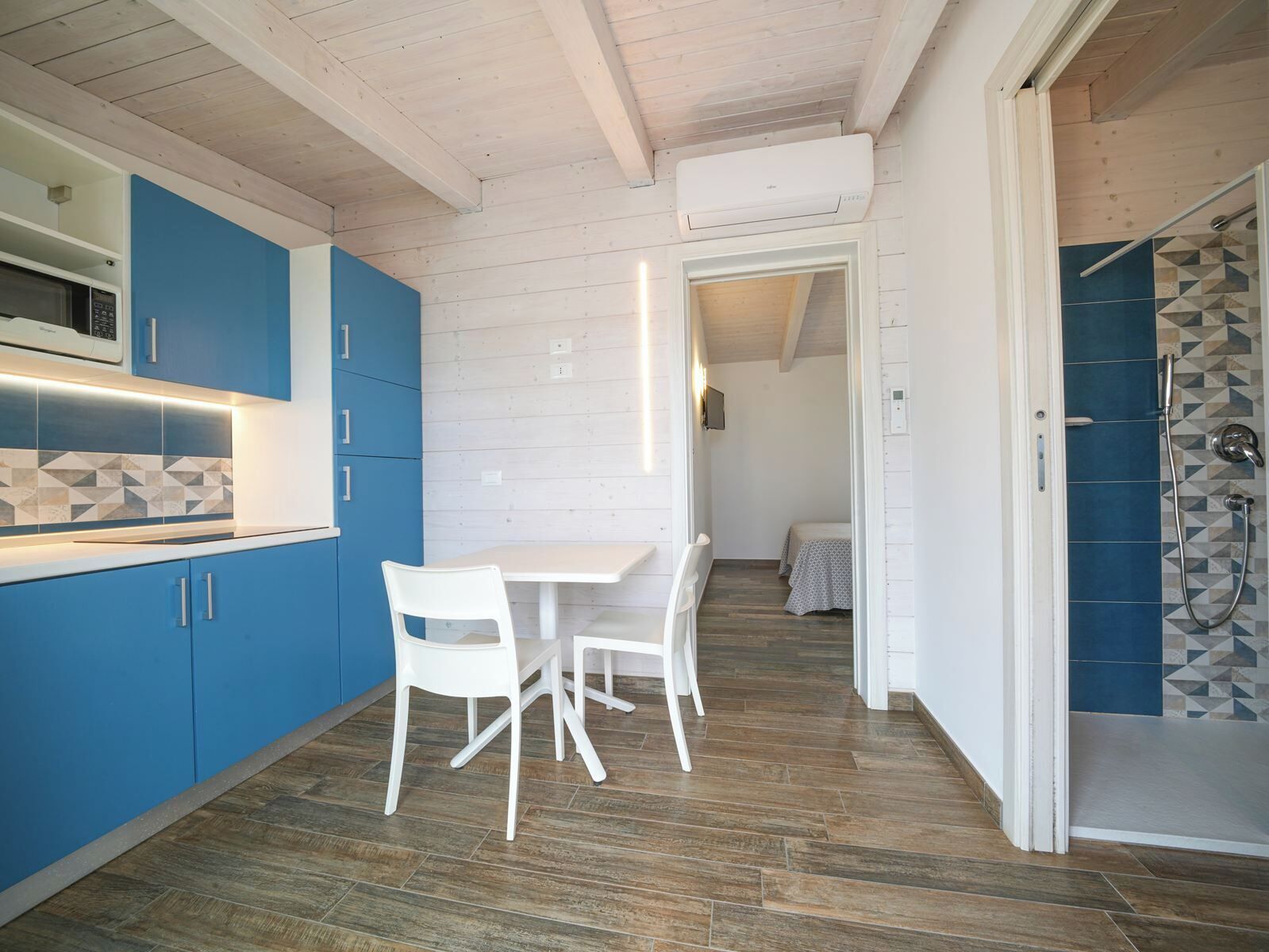 A modern kitchen with blue cabinets, a white dining table, and a wooden floor.