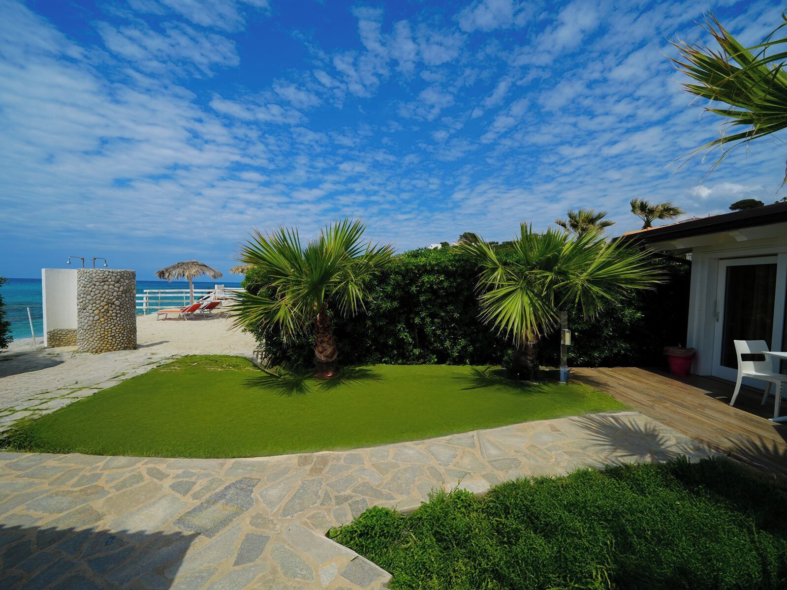 A beachside property with a stone pathway, a small lawn, and a palm tree.
