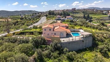 A large house with a swimming pool, surrounded by lush greenery and hills in the background.