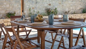 An outdoor dining area with a stone wall backdrop, wooden chairs, a round table, and a bowl of fruit. - Galini villa, private pool , near amenities, Heraklion (Episkopi)
