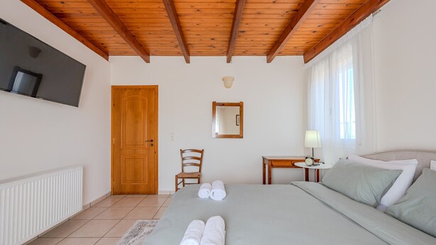 A bedroom with a wooden ceiling, a bed with neatly folded towels, a bedside table with a lamp, a chair, and a TV mounted on the wall. - Galini villa, private pool , near amenities, Heraklion (Episkopi)