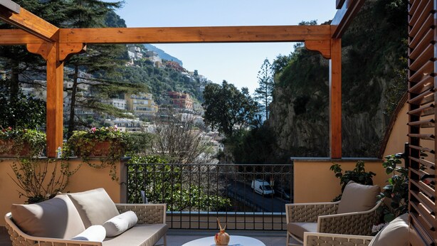 A balcony with wicker furniture, a white table, and a view of a mountainous town. - VILLA LEONARDO IN THE HEART OF POSITANO Central location (Positano)