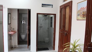 Ein Badezimmer mit Waschbecken, Toilette und Dusche. Ein Topf mit Pflanze und ein gerahmtes Bild sind an der Wand zu sehen.