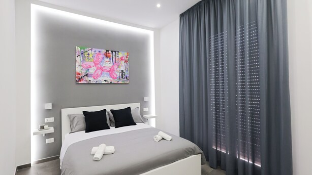 A modern bedroom with a large bed, a colorful abstract painting, and a grey curtain. - Napolitan Pop House (Naples)