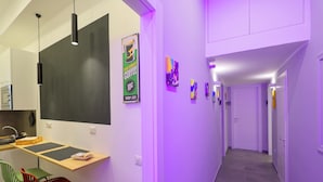 A modern kitchen with a dining area, a hallway with artwork, and a staircase. - Napolitan Pop House (Naples)