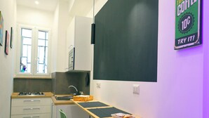 A narrow kitchen with a dining area, a blackboard, and a sign advertising coffee. - Napolitan Pop House (Naples)